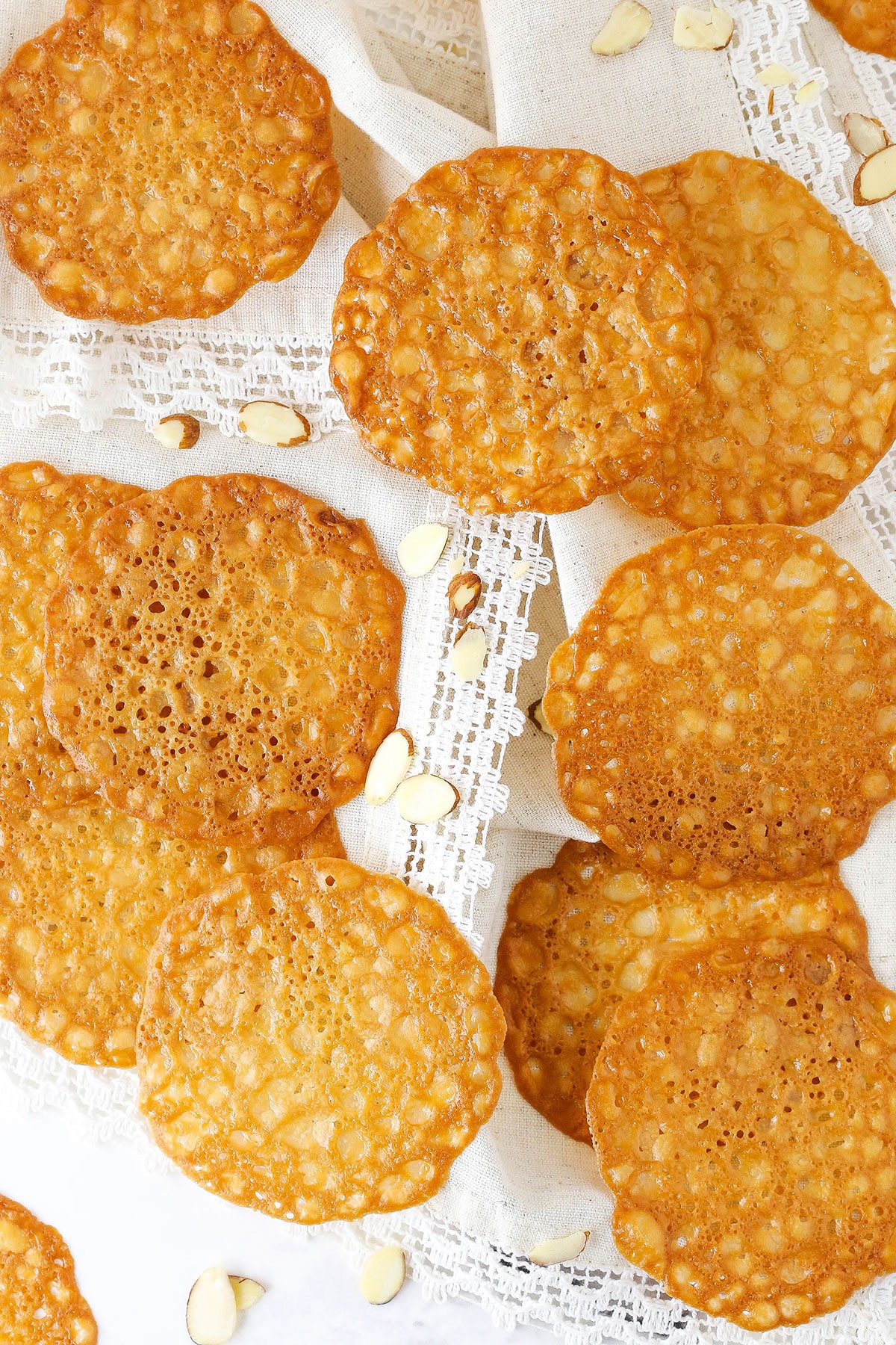 Lace Cookies Arranged on a Surface with White Doileys and Almond Slices