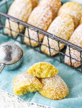 A Madeleine Tea Cake Broken in Half on a Teal Napkin with Other Cookies Nearby.