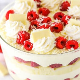 White chocolate raspberry trifle topped with swirls of whipped cream, fresh raspberries, and chocolate shavings.