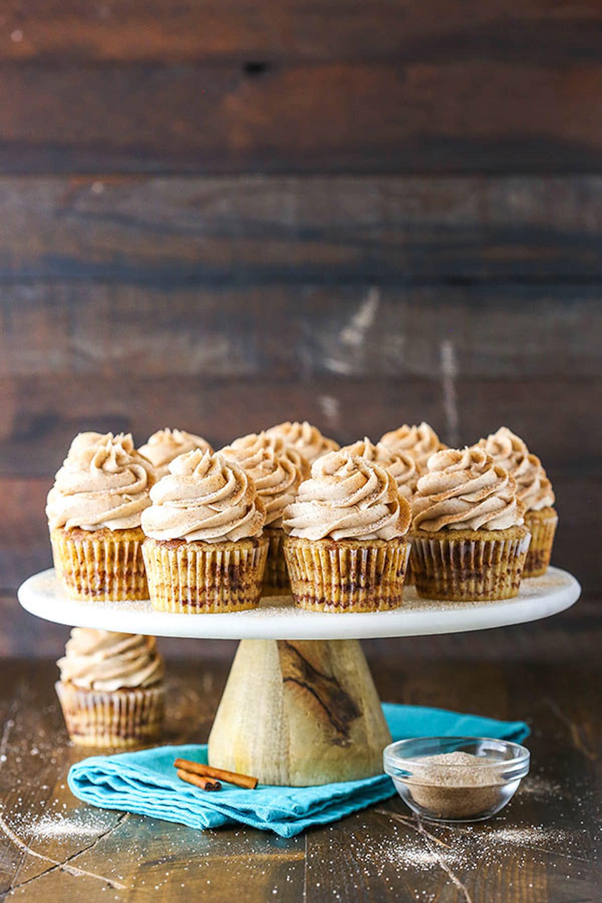 A Cake Stand Holding a Batch of Cinnamon Cupcakes in Front of a Wooden Wall