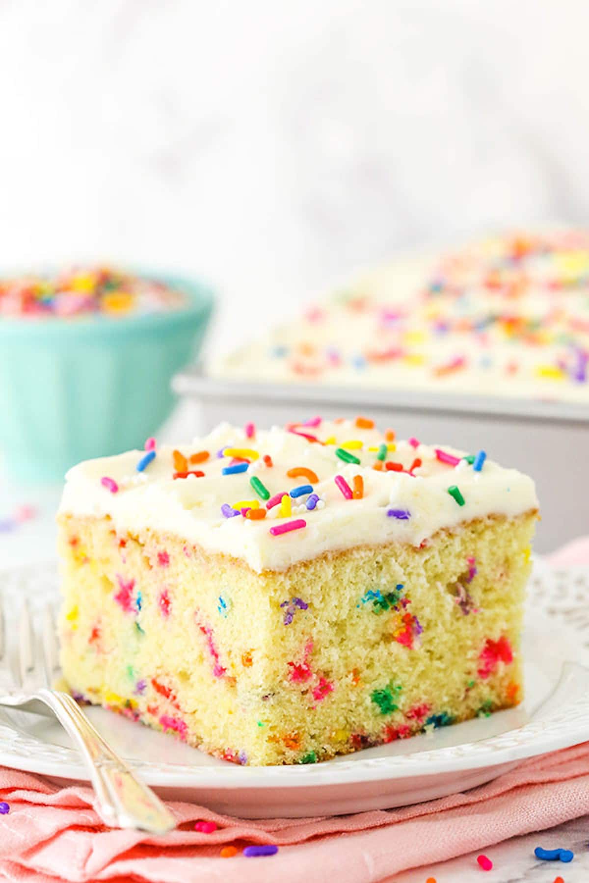 A Piece of Funfetti Cake on a Plate with the Rest of the Cake in the Background.