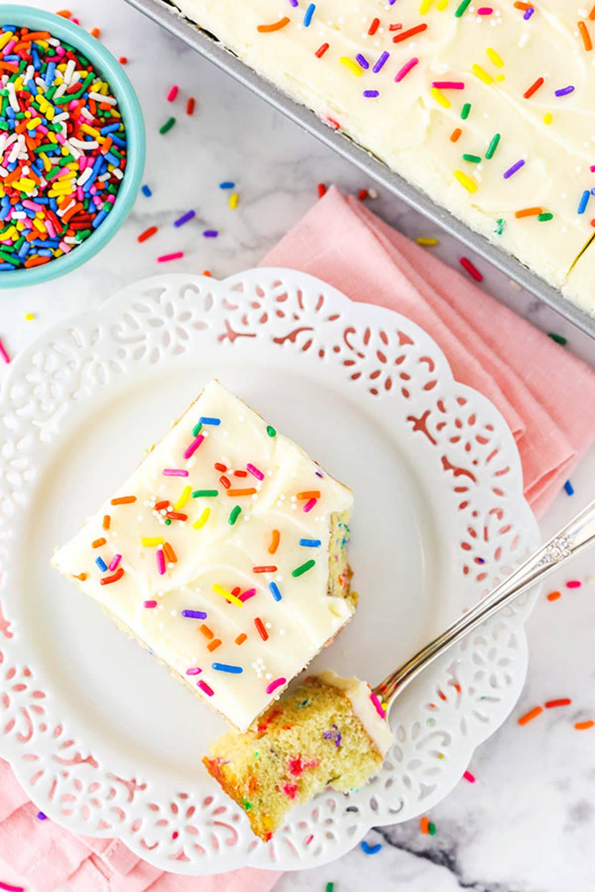 Overhead view of a piece of Funfetti Cake with vanilla frosting on a white plate.