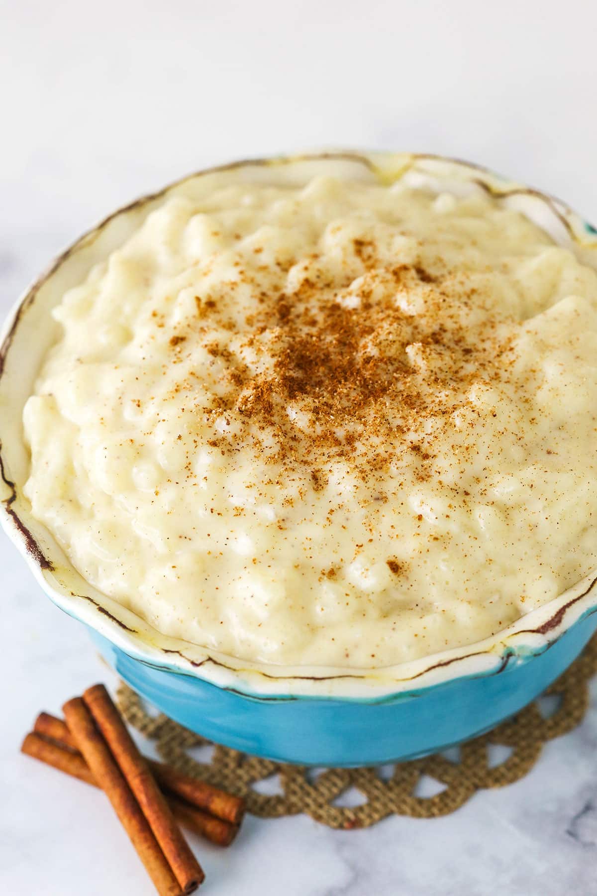 A Bowl of Rice Pudding Next to Two Cinnamon Sticks.