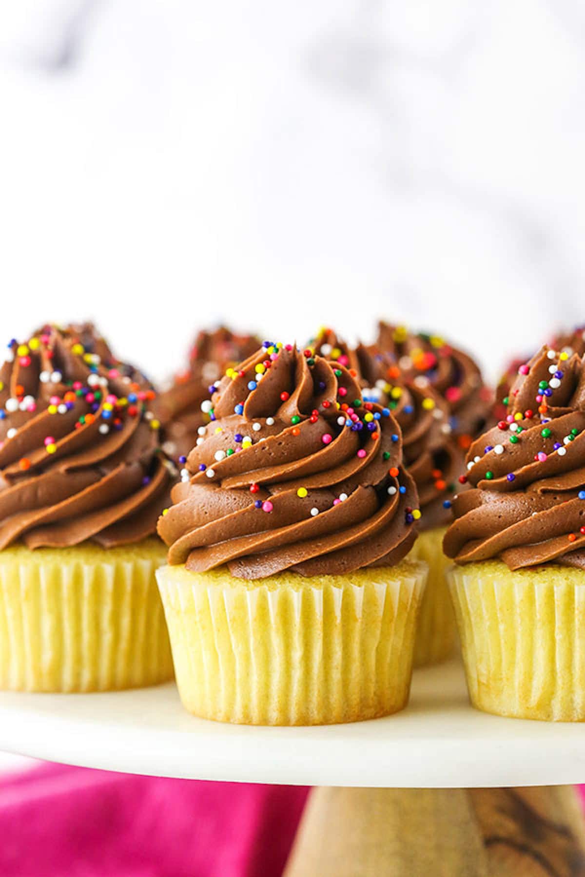 Side view of yellow cupcakes topped with chocolate frosting and rainbow sprinkles. 