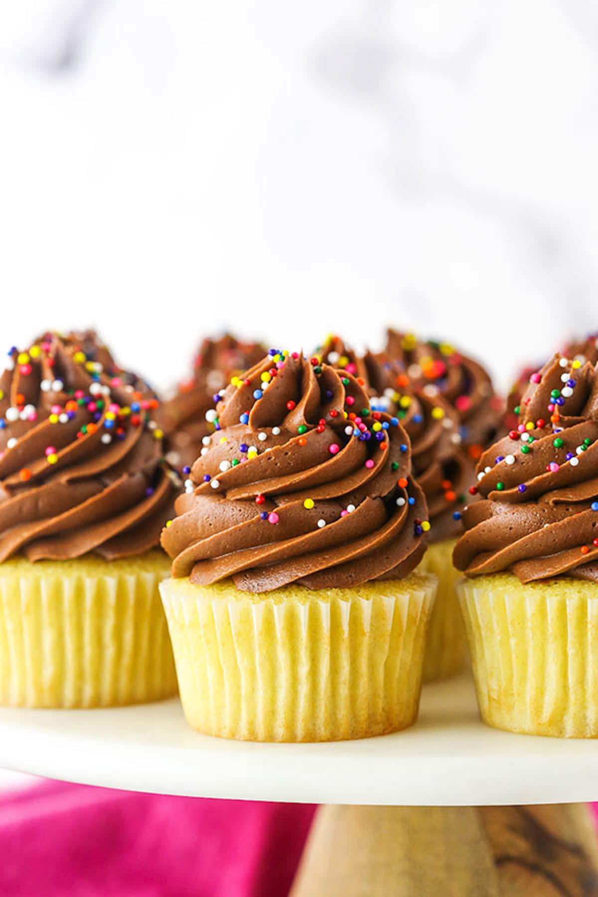 Side view of yellow cupcakes topped with chocolate frosting and rainbow sprinkles.