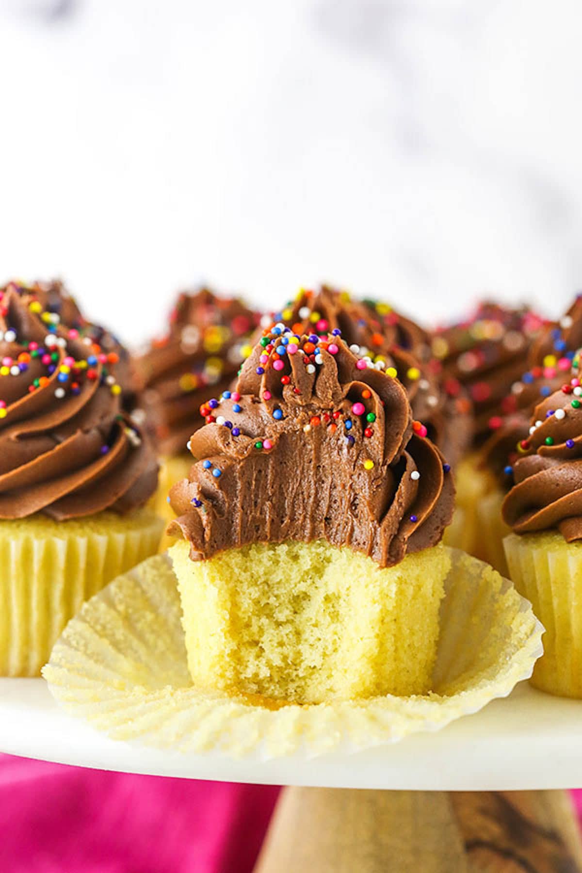 An unwrapped yellow cupcake with chocolate frosting and sprinkles on top with a bite taken out. 