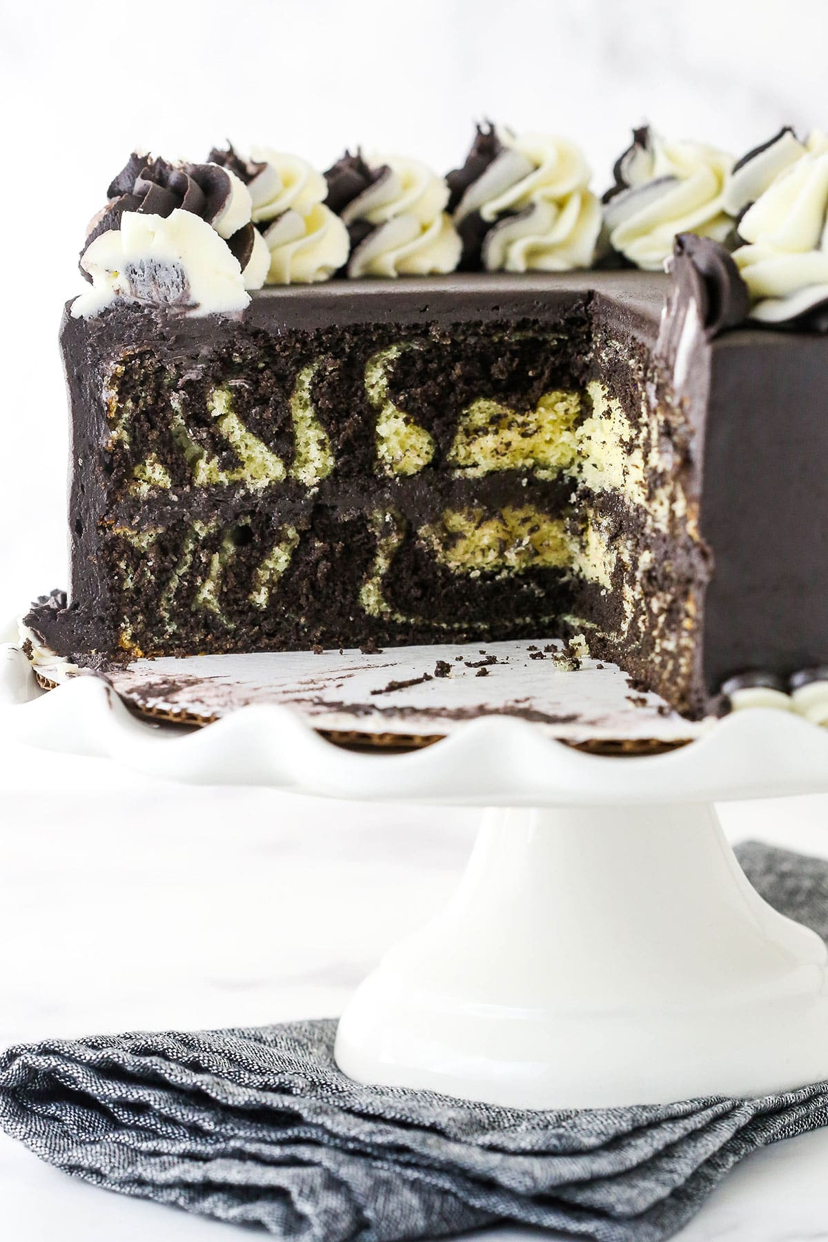 Side view of three quarters of a Zebra Layer Cake with vanilla and chocolate swirls on a dessert stand. 
