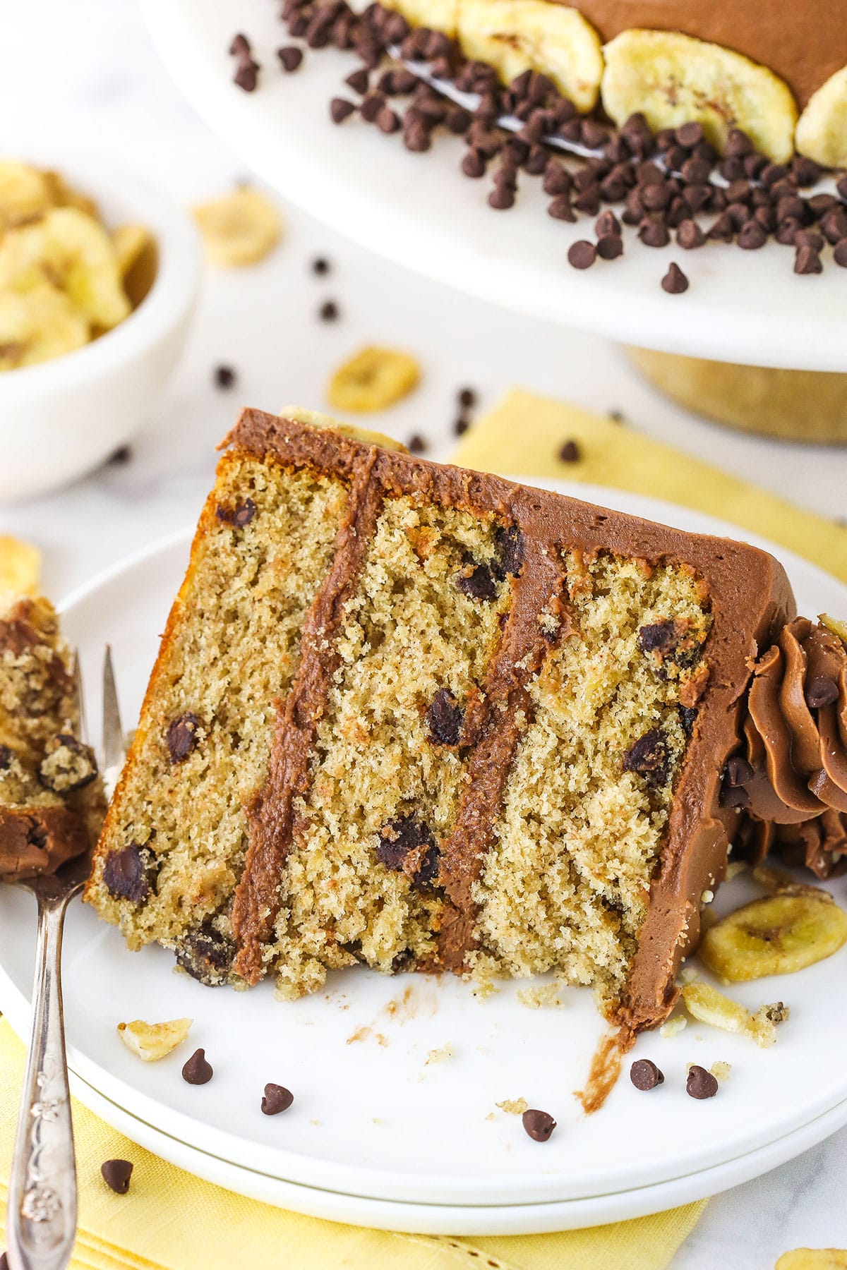 A slice of banana chocolate chip cake topped with chocolate frosting and chocolate swirls with a bite taken out.