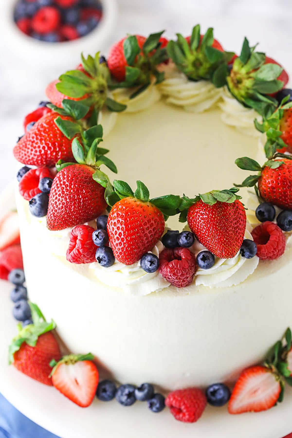 A Frosted Berry Chantilly Cake with a Ring of Strawberries, Blueberries and Raspberries on Top