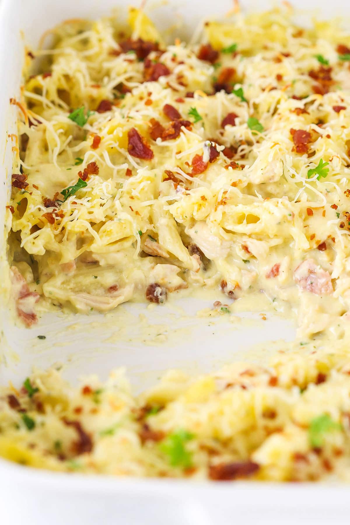 Close-up of chicken bacon ranch casserole with bacon bits and shredded cheese on top in a baking dish.