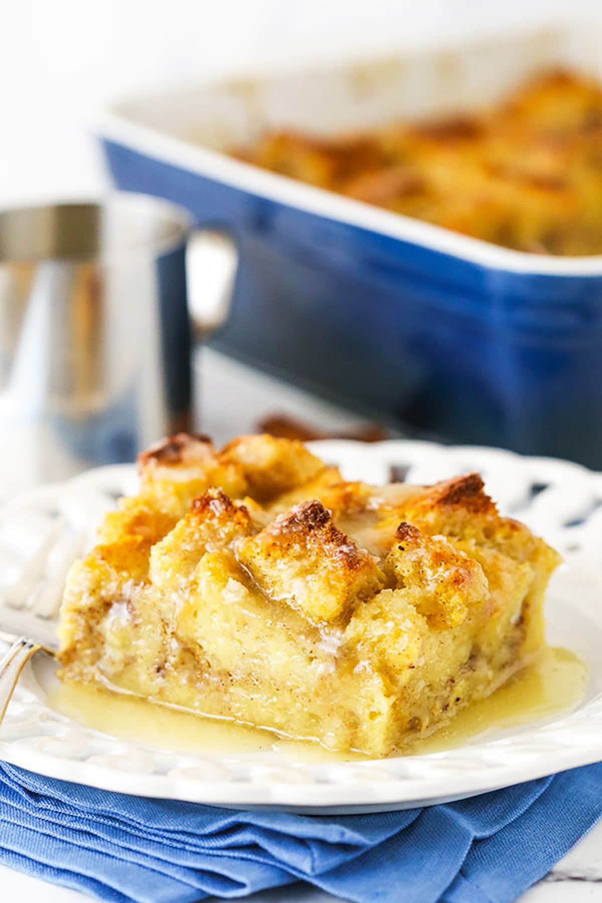 A square of bread pudding on a plate with the rest of the pudding in the background.