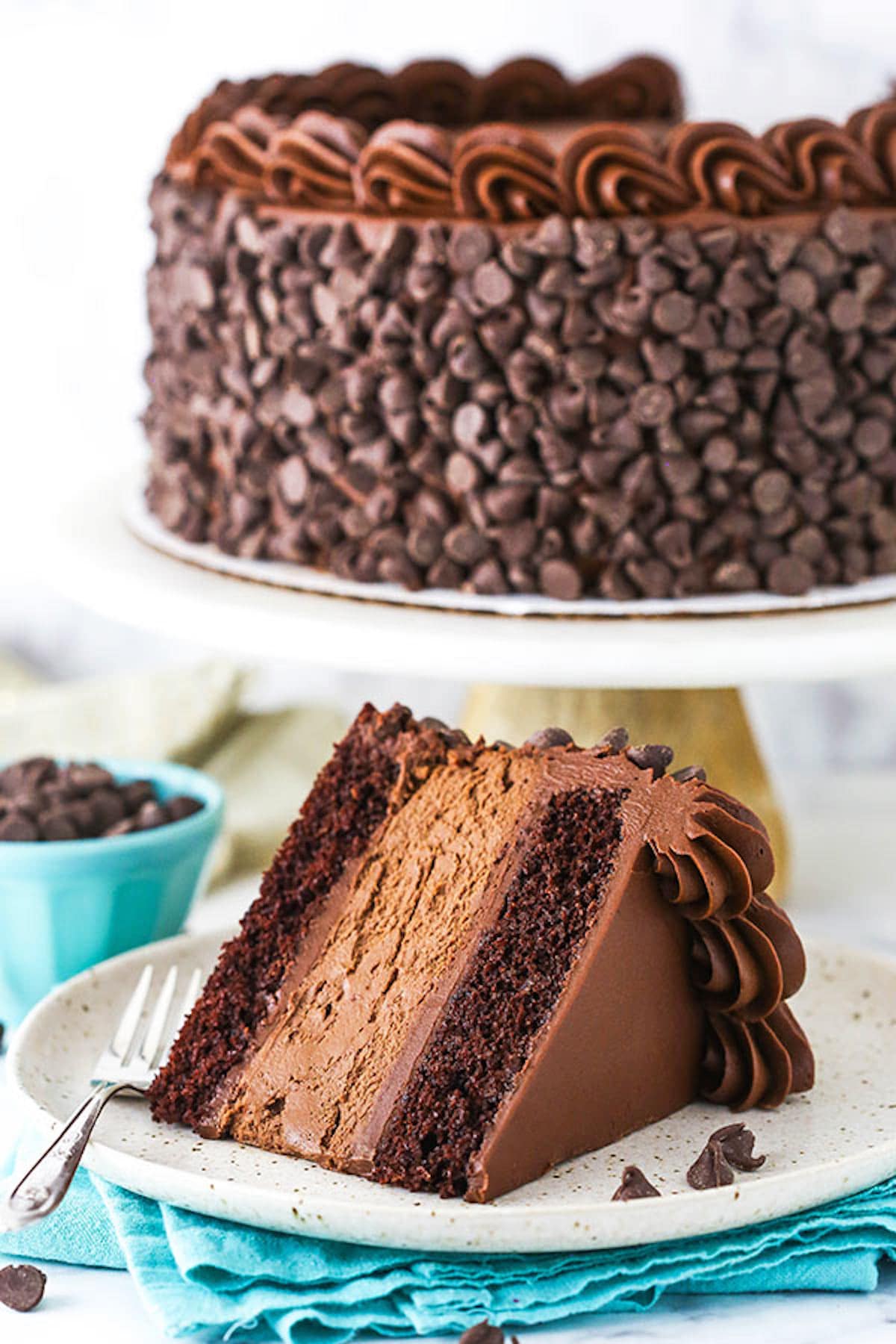 A Slice of Chocolate Layer Cake Next to the Rest of the Cake on a Cake Stand