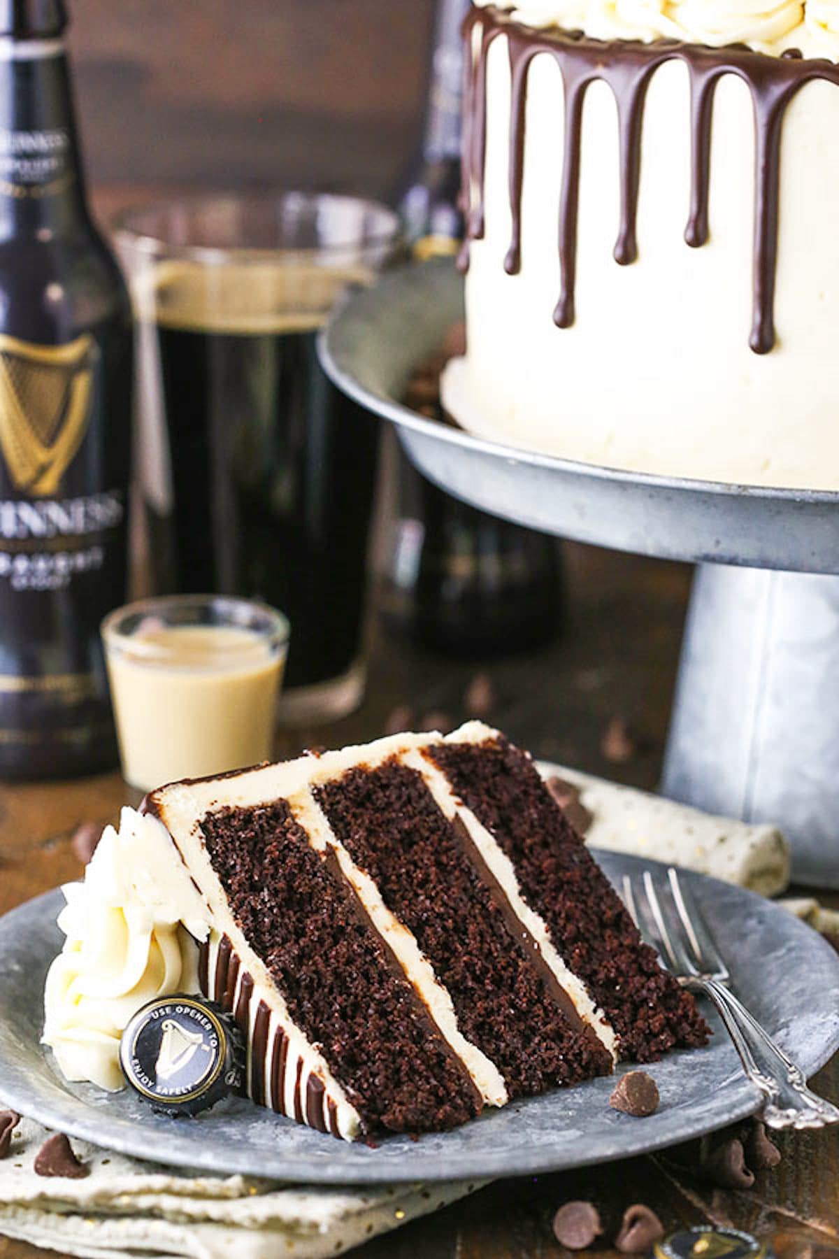 A Slice of Layer Cake on a Plate in Front of the Rest of the Cake on a Cake Stand