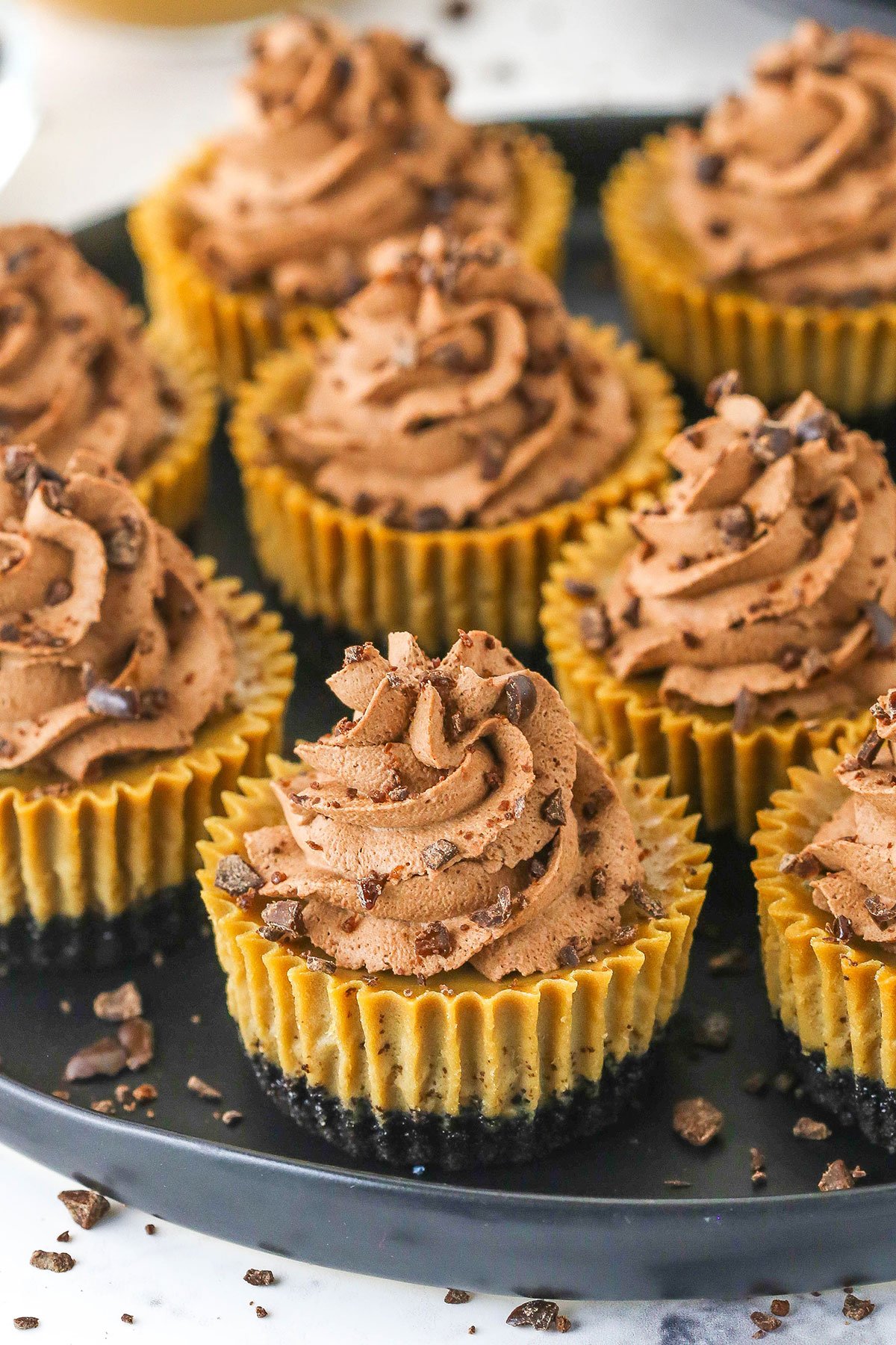 A plate full of mini coffee cheesecakes garnished with crushed chocolate covered espresso beans.