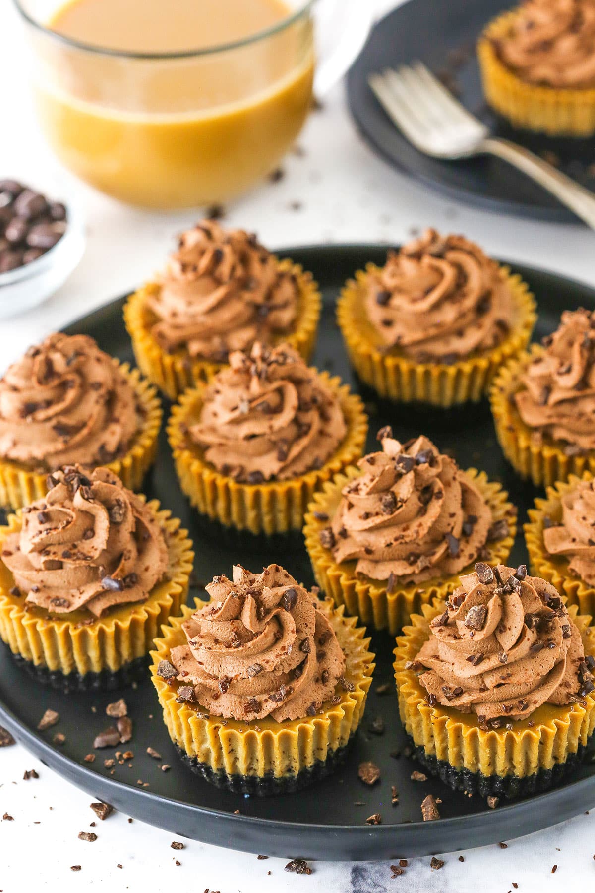 Overhead view of ten mini coffee cheesecakes on a round black serving dish. 