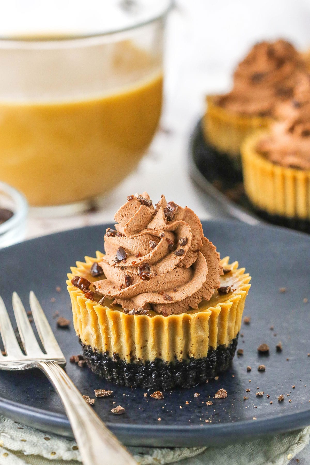 Side view of a mini coffee cheesecake topped with a chocolate swirl and chocolate chip bits on a black plate. 