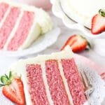 A Piece of Strawberry Cake on a Plate with a Sliced Strawberry Beside It