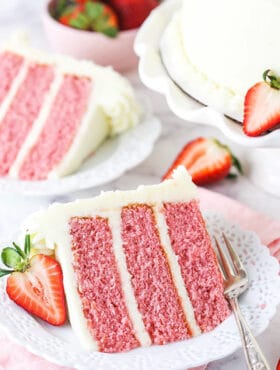 A Piece of Strawberry Cake on a Plate with a Sliced Strawberry Beside It