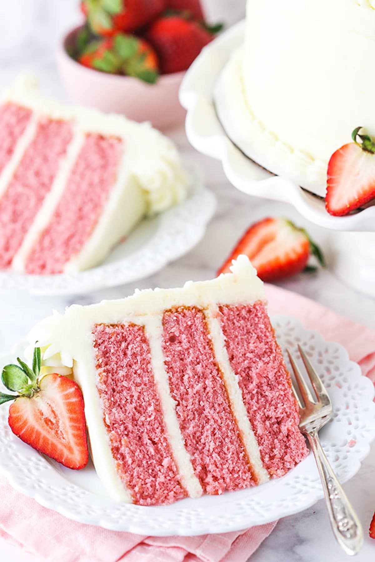 A Piece of Strawberry Cake on a Plate with a Sliced Strawberry Beside It