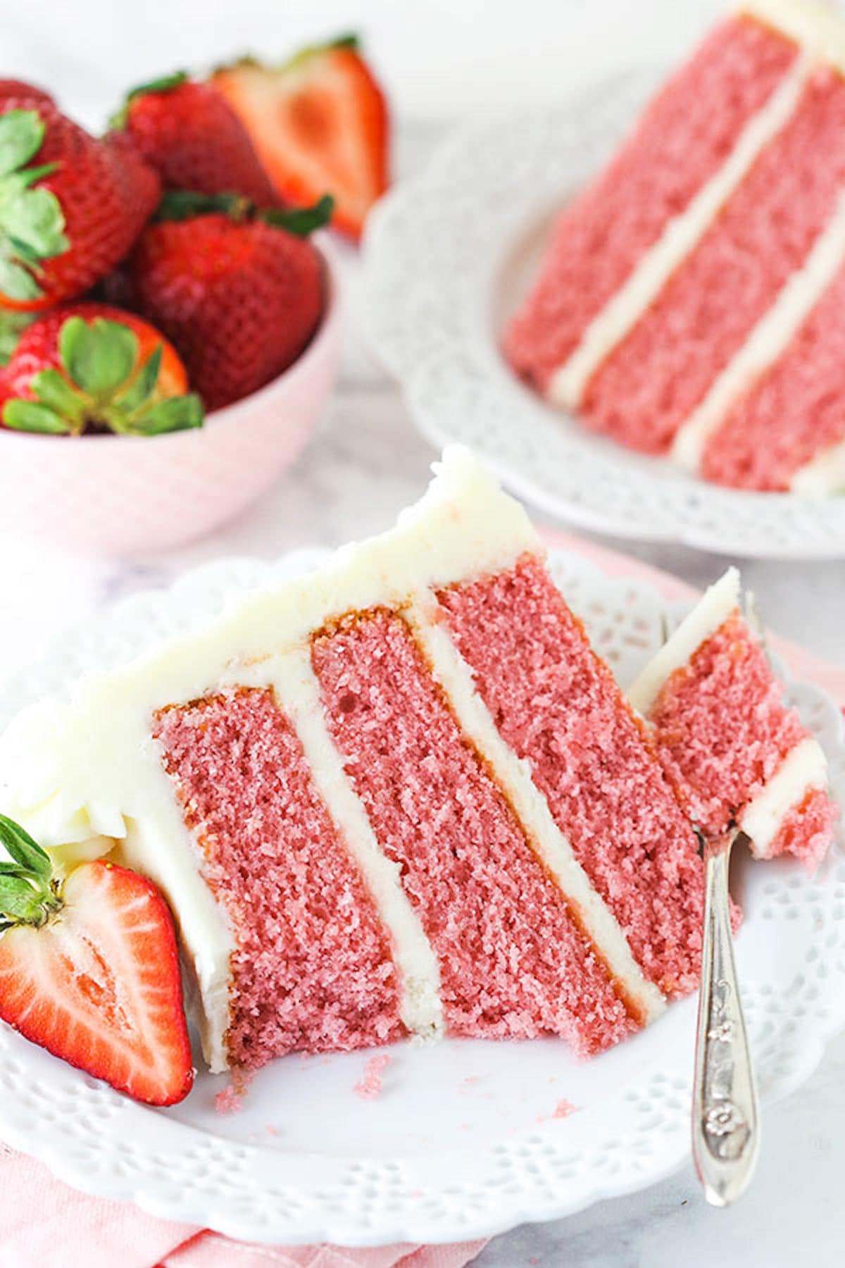 A Piece of Strawberry Layer Cake on a Plate with One Bite on a Fork
