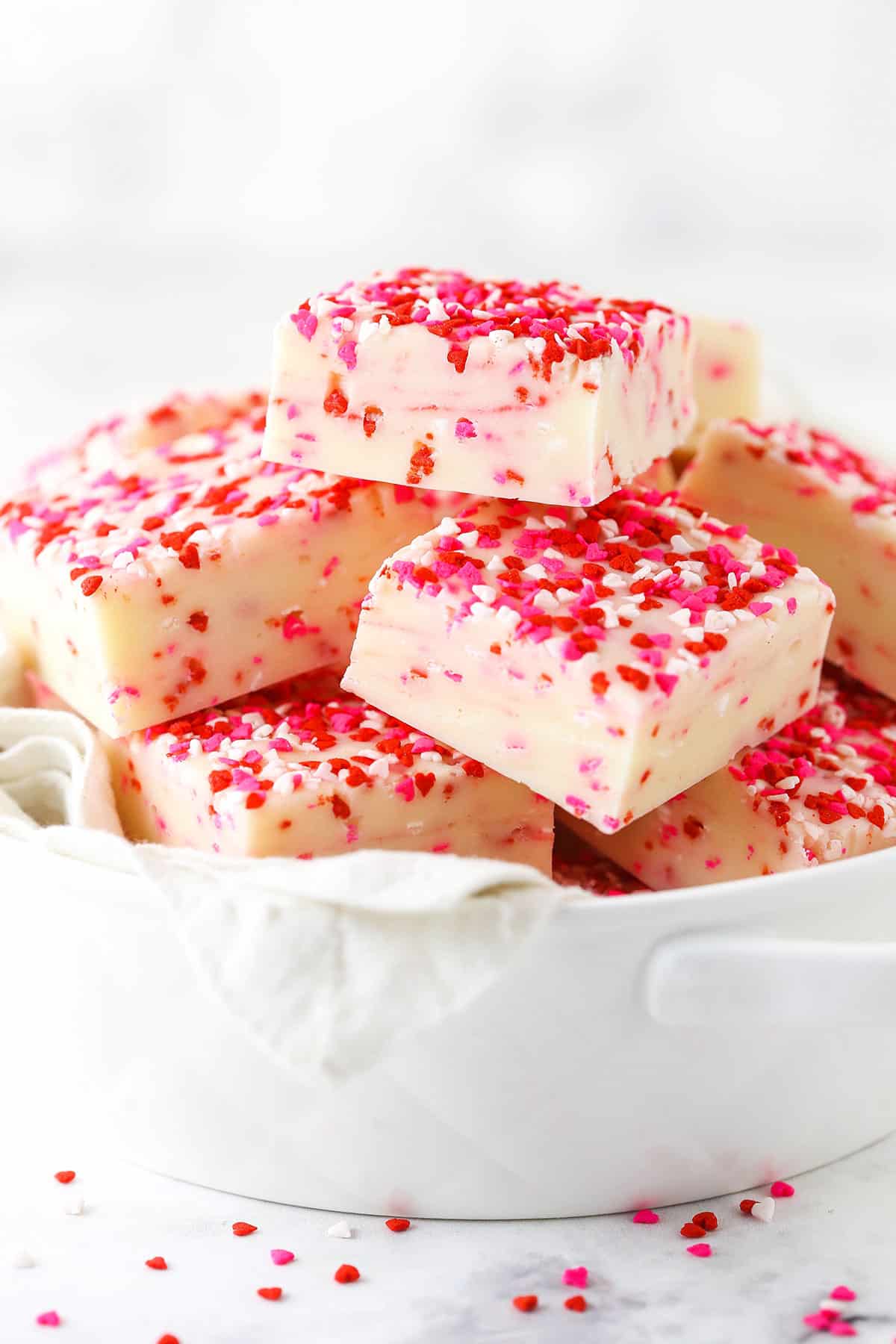 Valentine's Day Fudge squares with white, pink and red sprinkles piled in a white bowl.