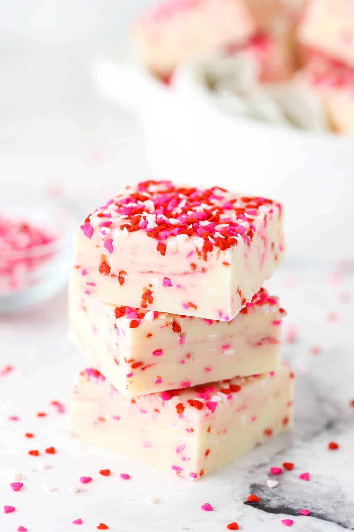Side view of three squares of Valentine's Day fudge with red, white and pink sprinkles stacked on top of each other. 