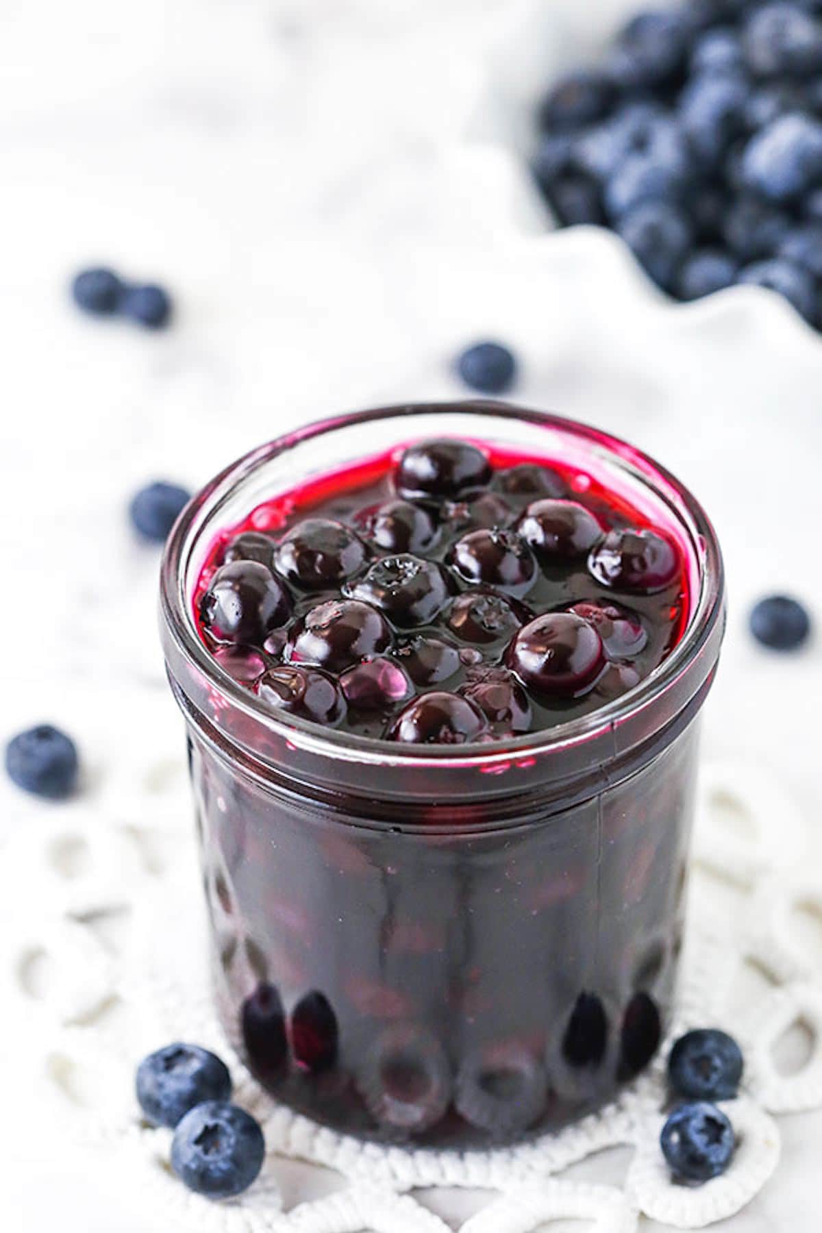A Close-Up Shot of Homemade Blueberry Sauce in a Glass Jar Next to a Few Fresh Blueberries