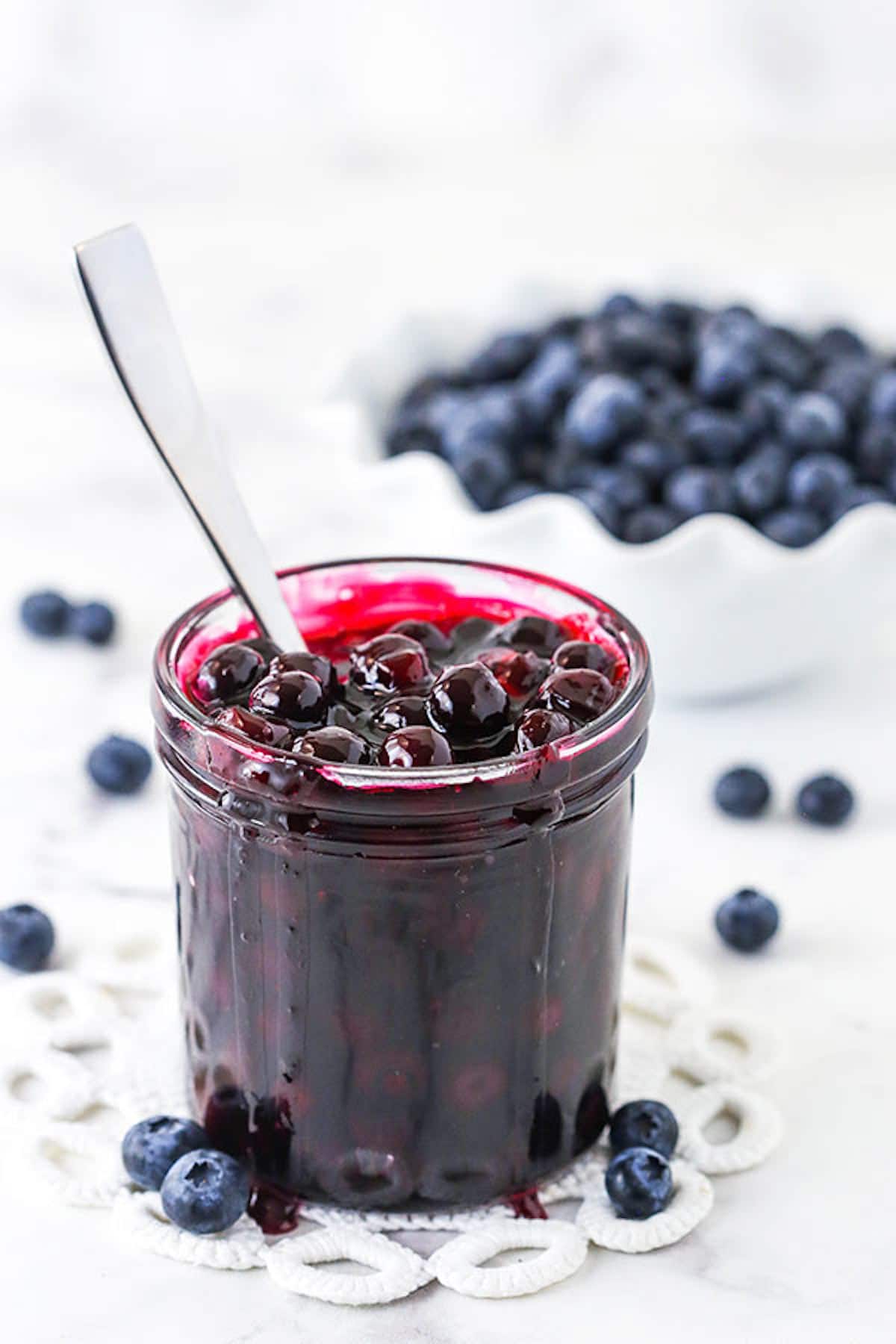 A Glass Jar of Blueberry Sauce in Front of a Bowl of Fresh Blueberries