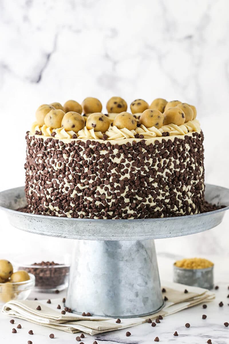 A Cake Stand on a Counter Holding a Decorated Chocolate Chip Cookie Dough Cake