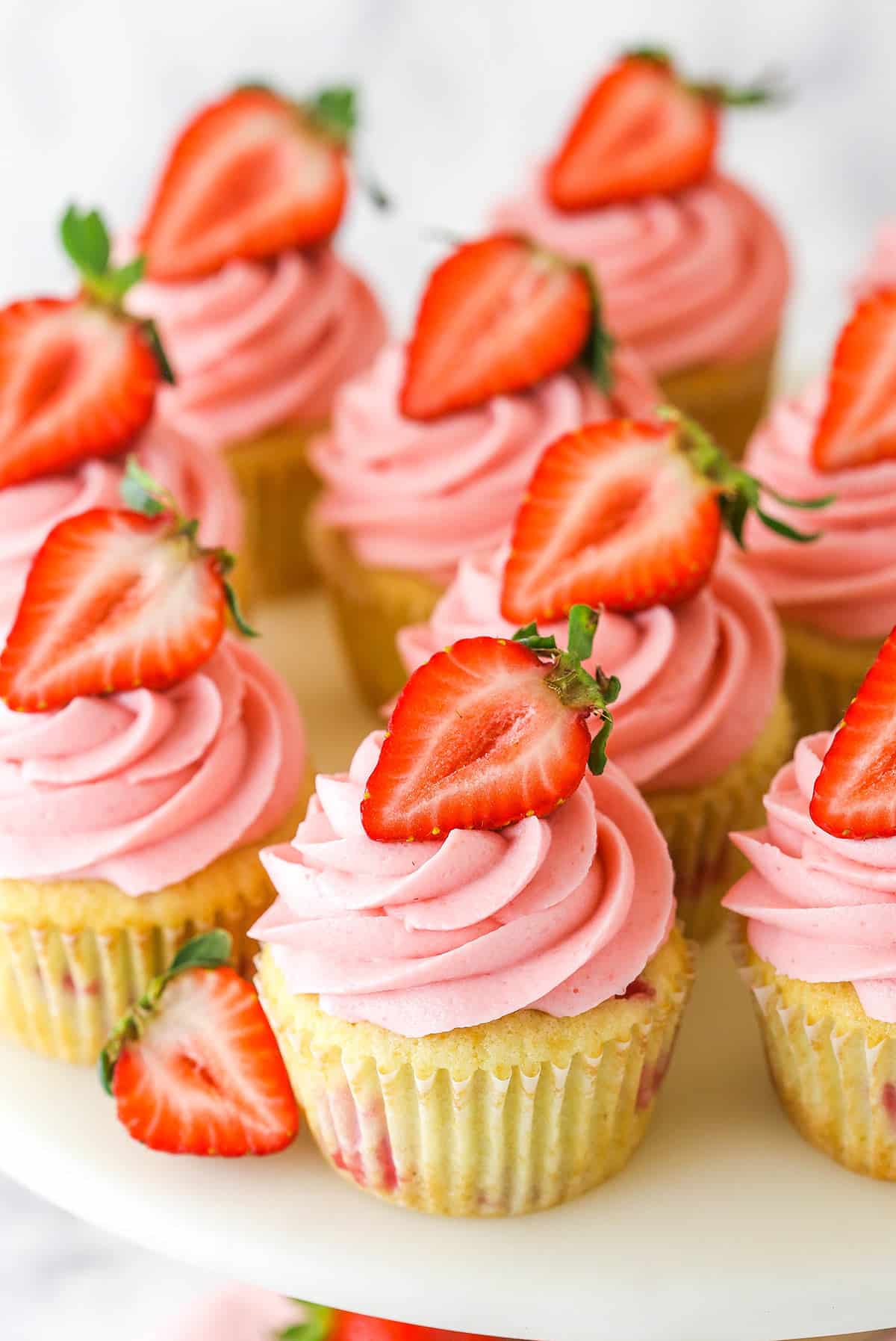 overhead angled image of strawberry cupcakes with a strawberry half tucked beside one
