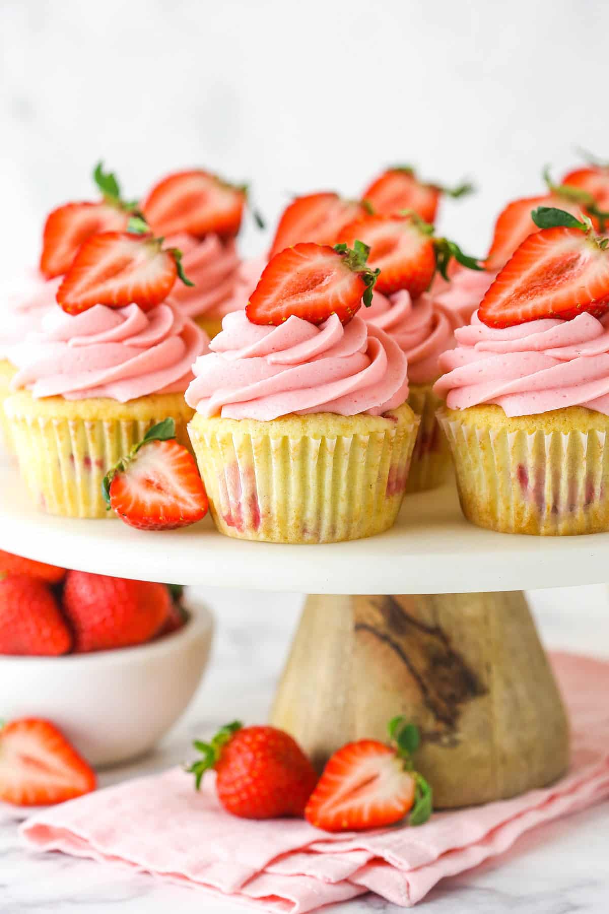 fresh strawberry cupcakes on marble and wood cake stand with strawberries around base