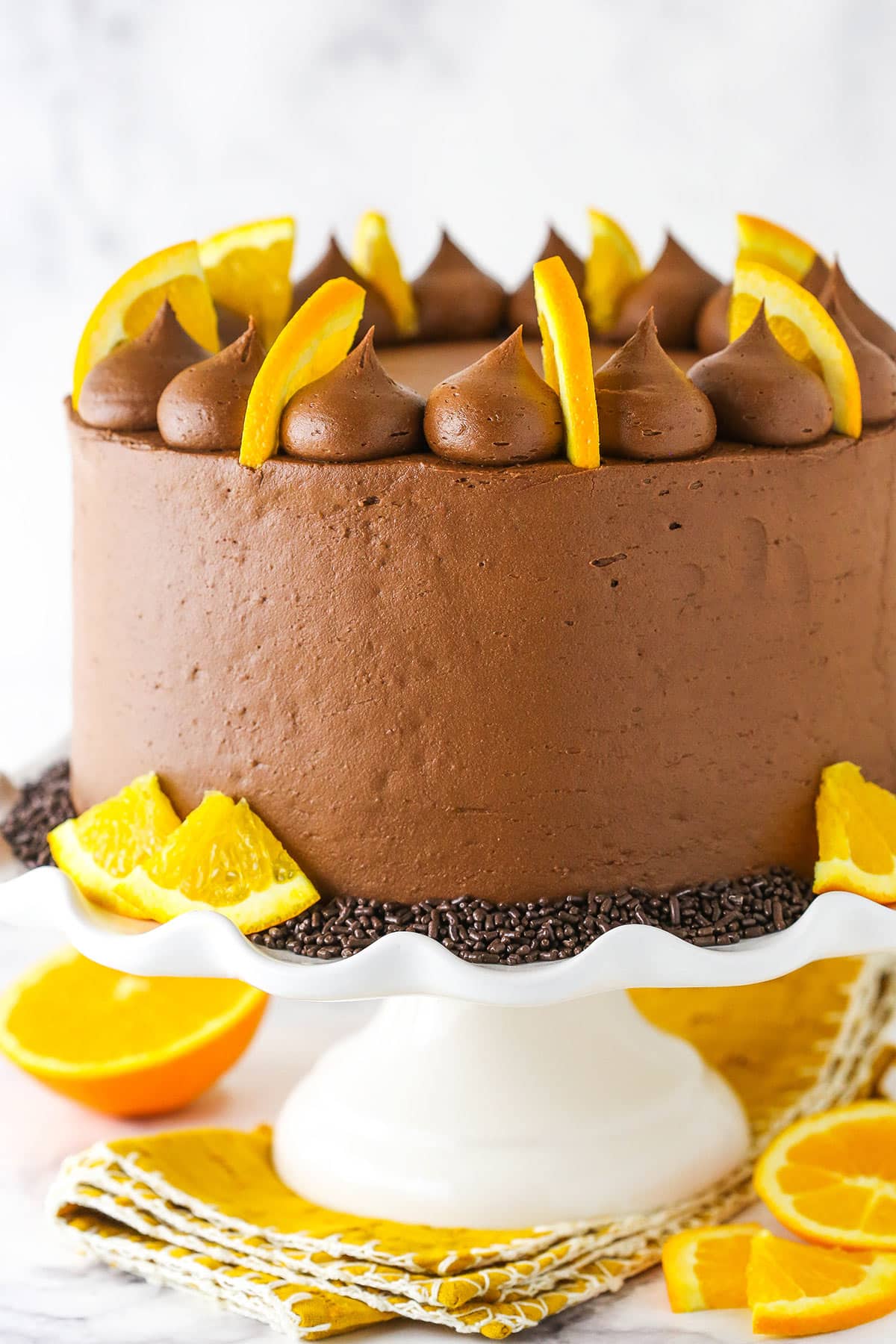 full orange chocolate cake on a white cake stand with orange slices