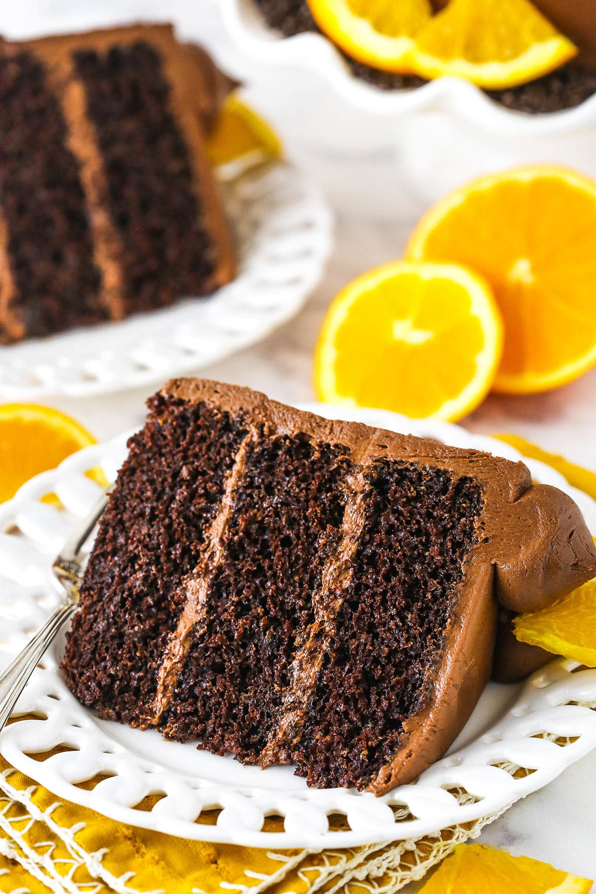 two orange chocolate cake slices on white plates with oranges in background