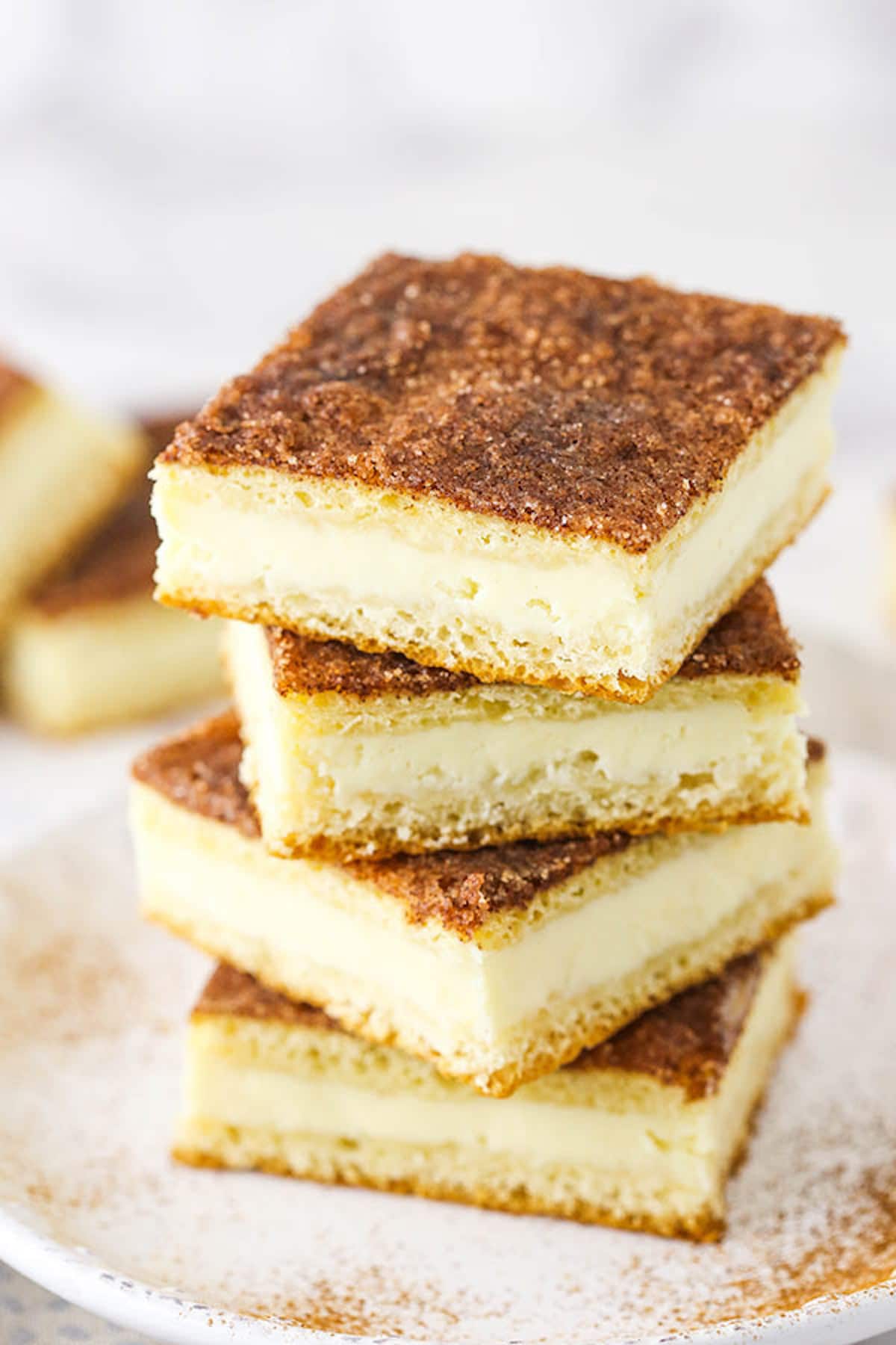 These easy Sopapilla Cheesecake Bars are truly incredible! Made with crescent dough, creamy cheesecake filling & cinnamon sugar topping. A Pile of Sopapilla Bars on a Plate Dusted with Cinnamon Sugar