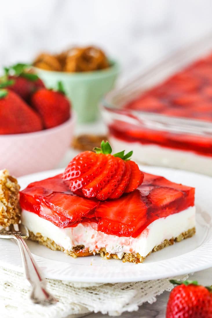 A slice of strawberry pretzel salad on a white plate, with a bite missing