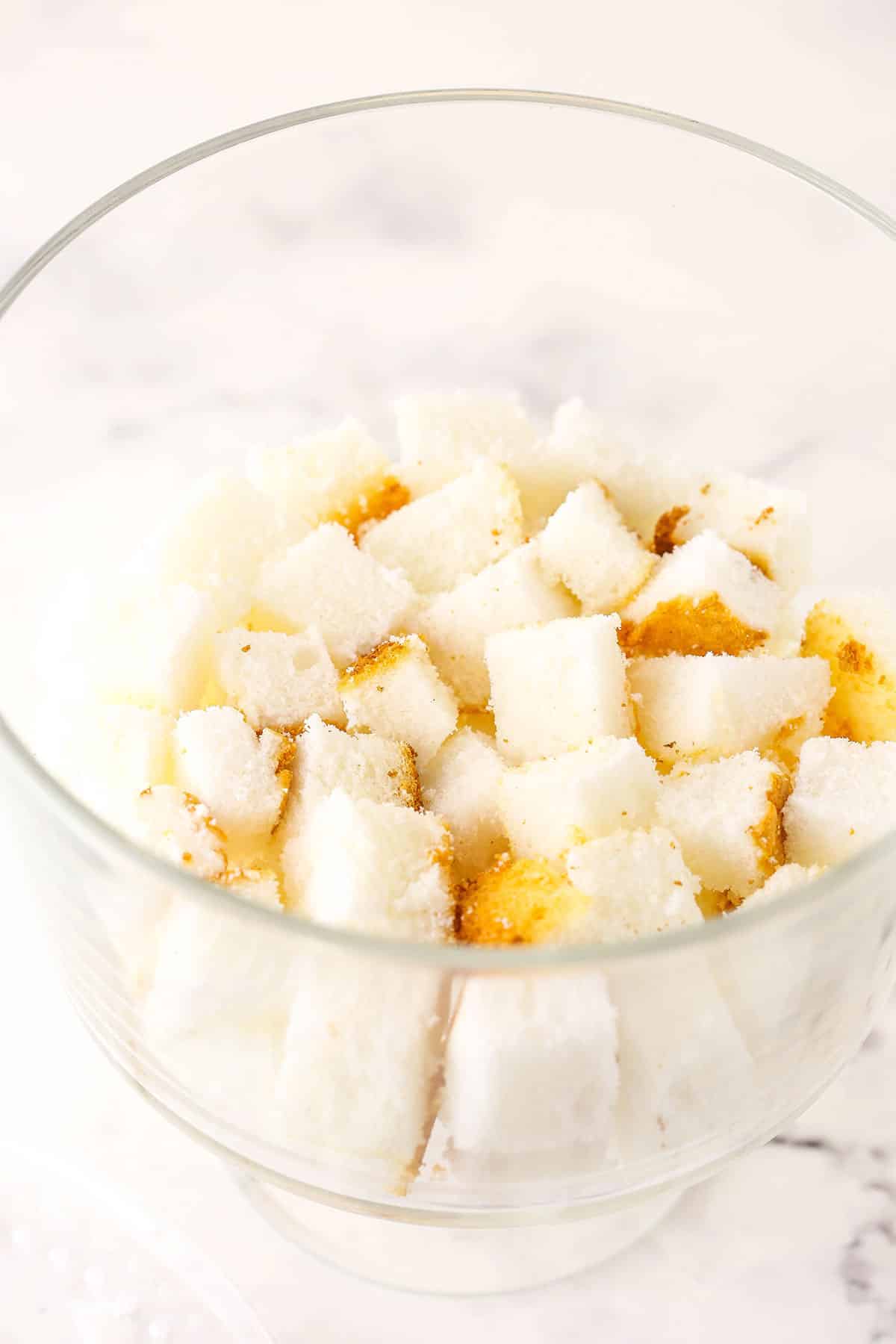 Overhead view of angel food cake cut into cubes in a glass trifle bowl.