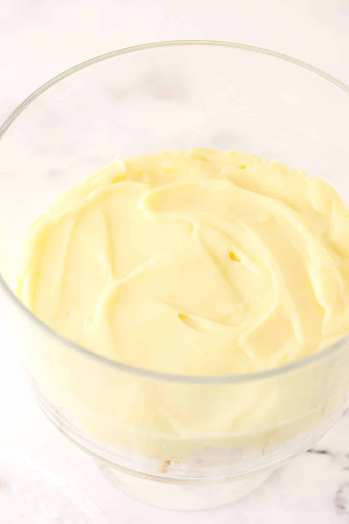 Pudding mixture on top of angel food cake in glass trifle bowl.