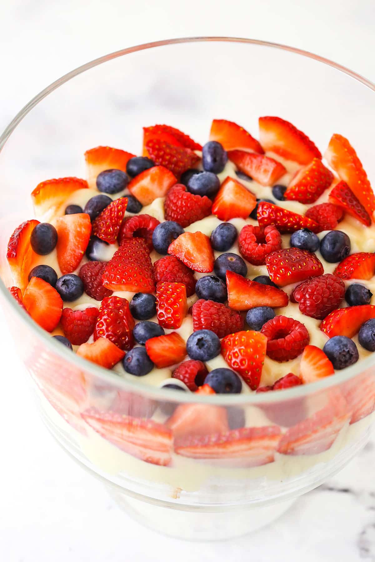 Overhead view of strawberries, raspberries and blueberries being added on top of trifle pudding layer.