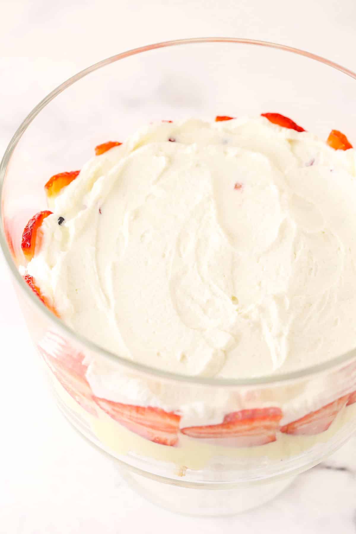 Overhead view of whipped cream being added on top of trifle berries layer.