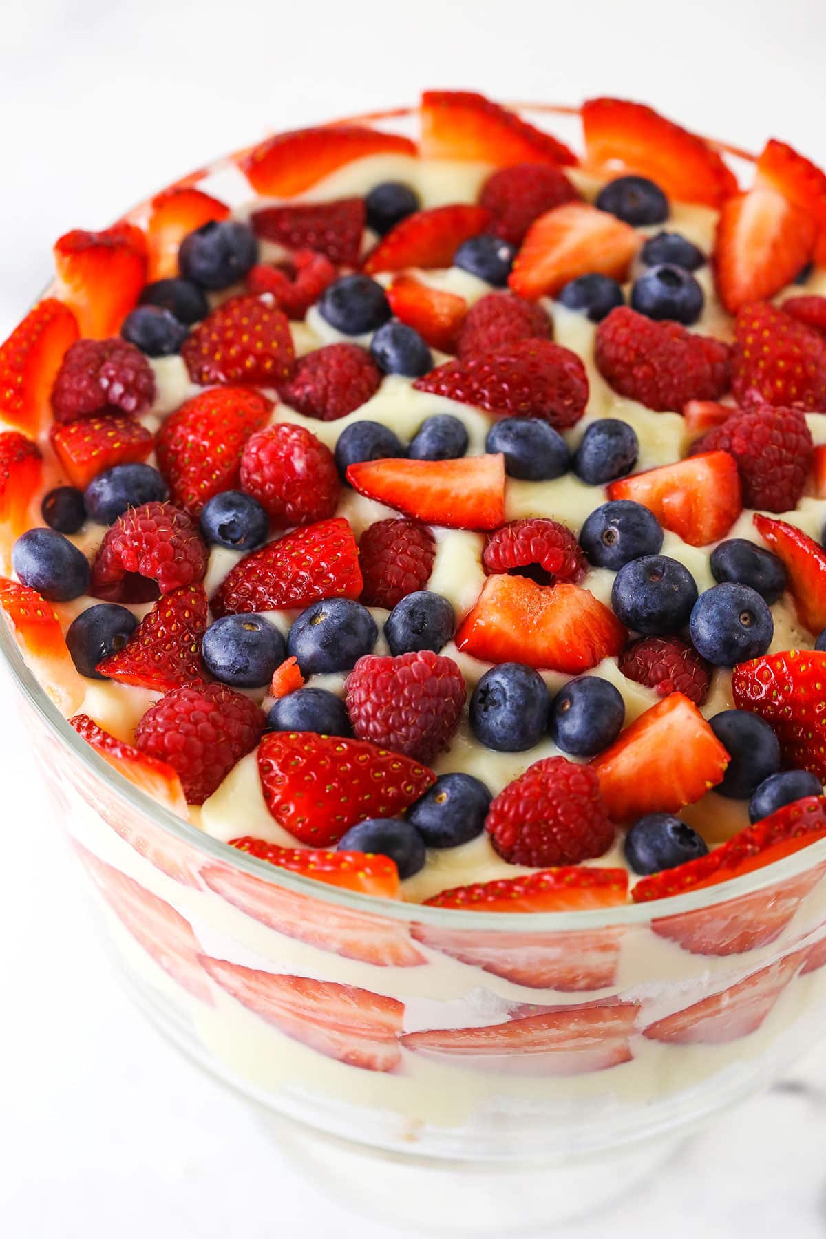 Overhead view of final layer of strawberries, raspberries and blueberries being added on top of trifle pudding layer.