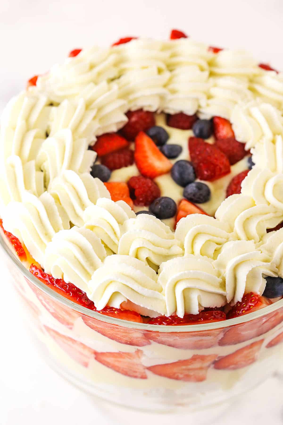 This trifle recipe is the best summer dessert! It's filled with layers of angel food cake, pudding, strawberries, blueberries & raspberries. layered trifle with piped whipped cream on top in trifle bowl