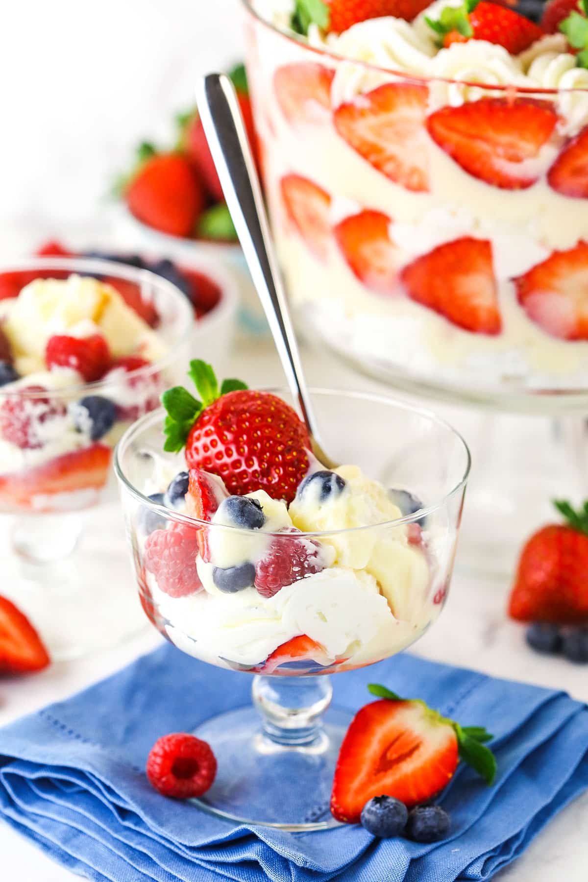 This trifle recipe is the best summer dessert! It's filled with layers of angel food cake, pudding, strawberries, blueberries & raspberries. A scoop of triple berry trifle in a mini trifle dish with a spoon in it