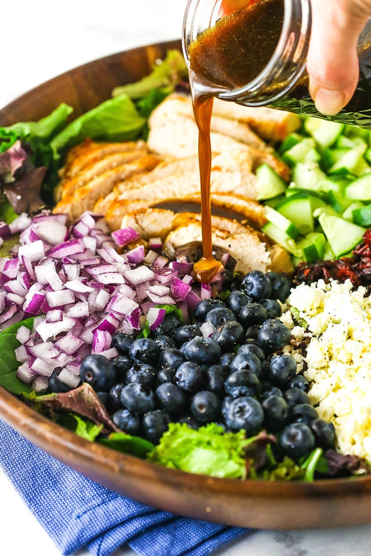 Balsamic vinaigrette being poured over a bowl over chicken blueberry feta salad