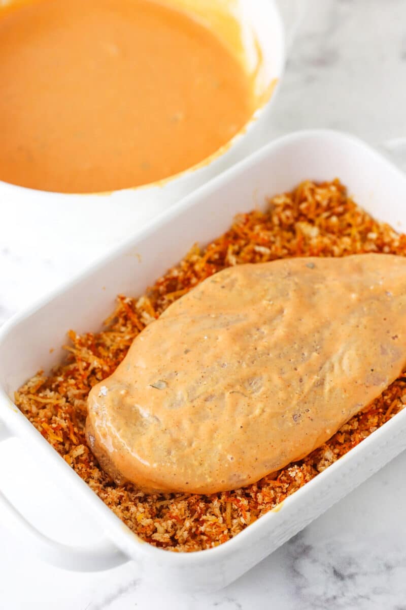 Buffalo and ranch coated chicken sitting in a white dish full of panko mixture