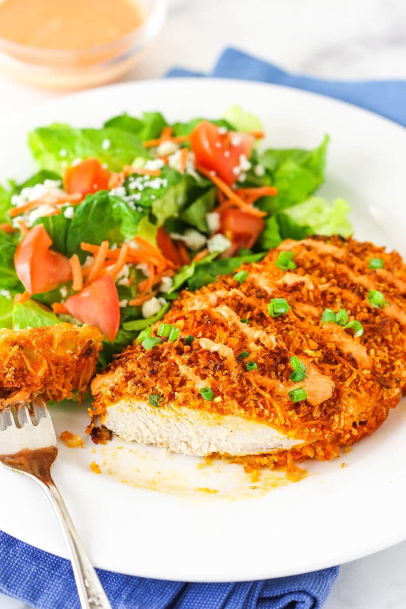 Buffalo Chicken on white plate with salad and a bit taken out of chicken.