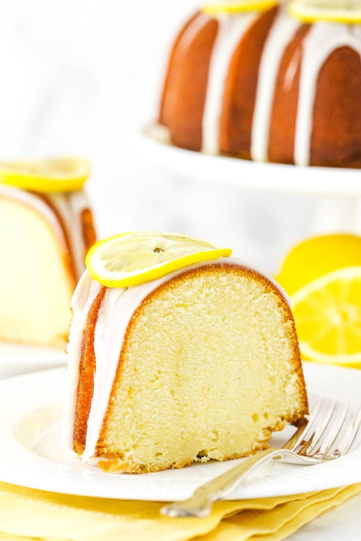 A slice of lemon pound cake on a white plate, garnished with a lemon slice.