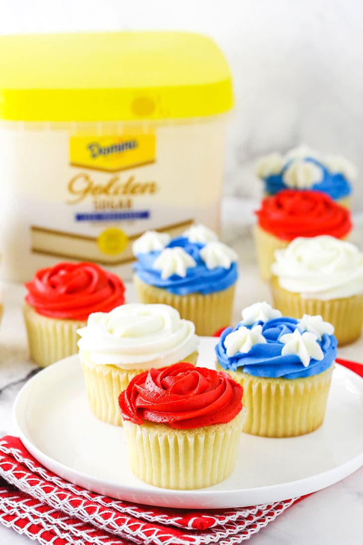 three cupcakes on a white plate with golden sugar package in background