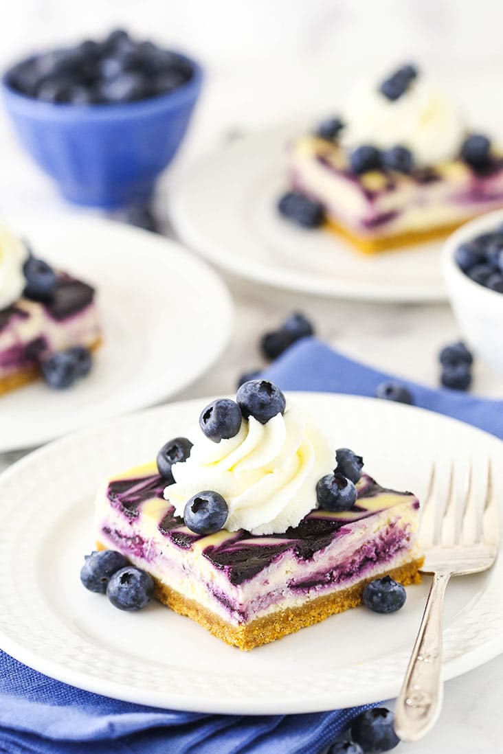 A slice of blueberry swirl cheesecake topped with whipped cream and blueberries