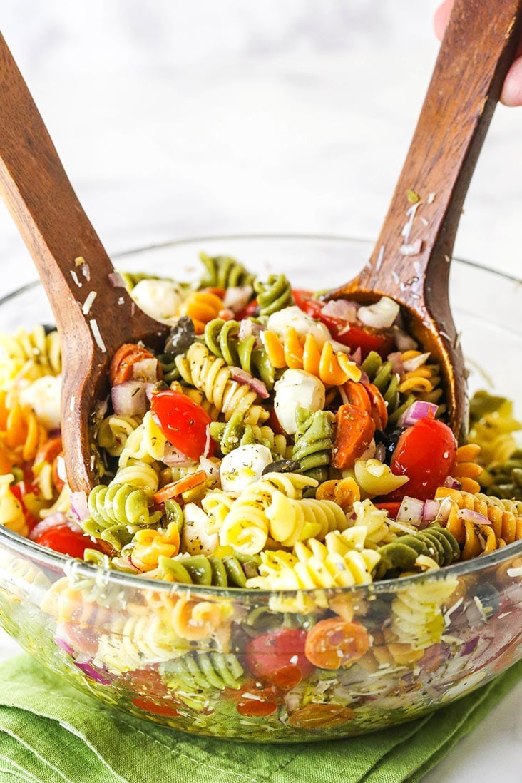 Two wooden spoons mixing a big bowl of Italian pasta salad