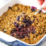 blueberry crisp in casserole dish with a scoop being taken out